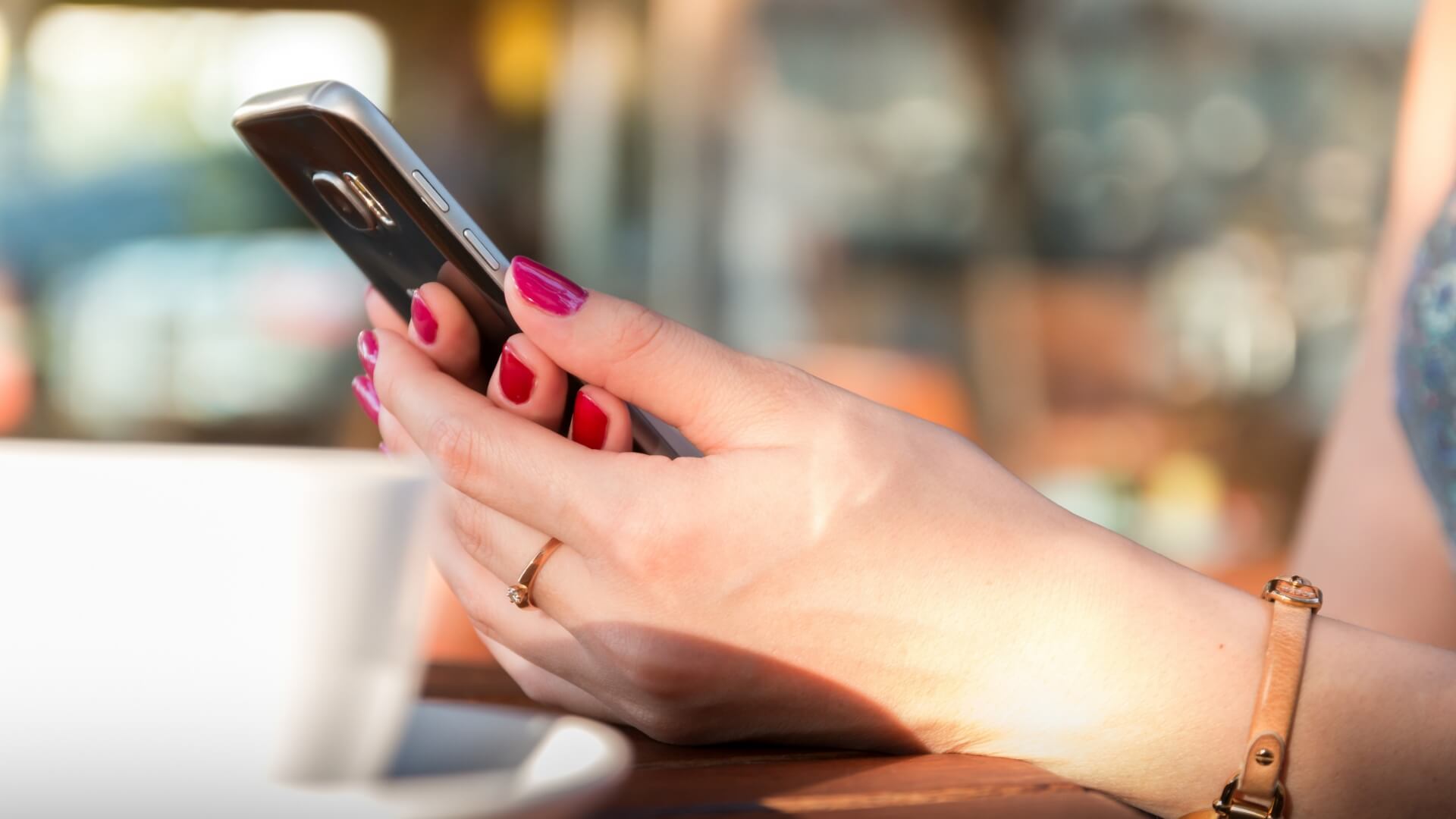 Woman holding her android device with a coffee cup beside her