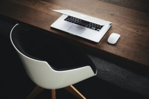Apple macbook on a wooden table with desk mouse and chair