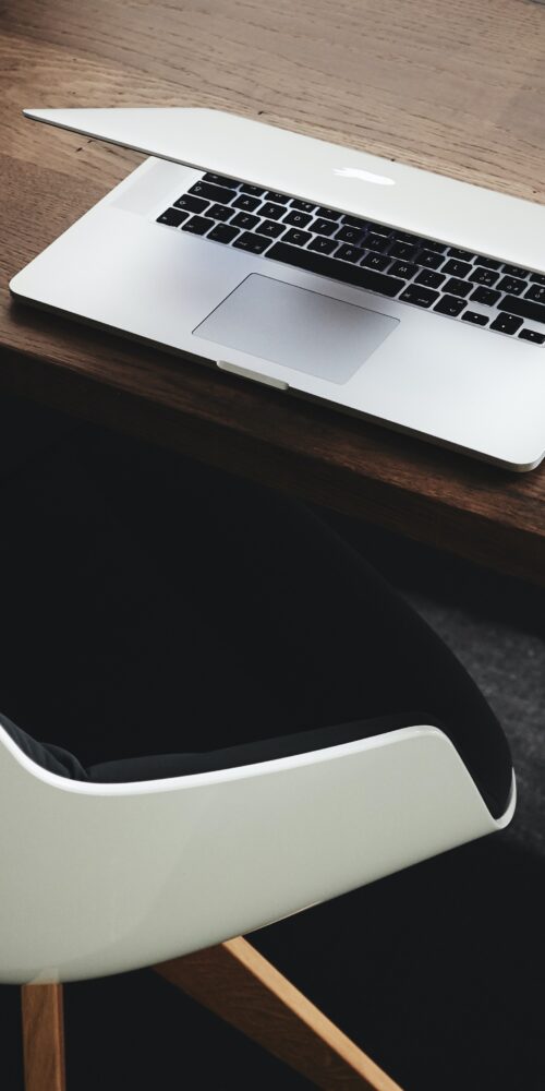 Apple macbook on a wooden table with desk mouse and chair